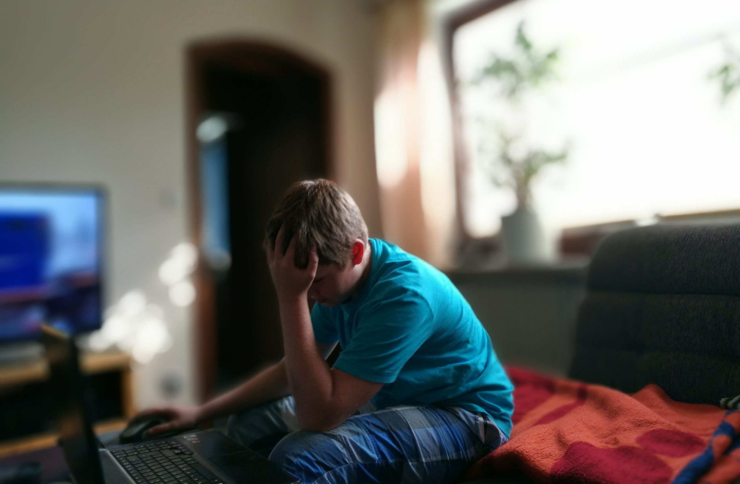 Frustrated Teenage Boy Using Laptop With Head In Hand At Home