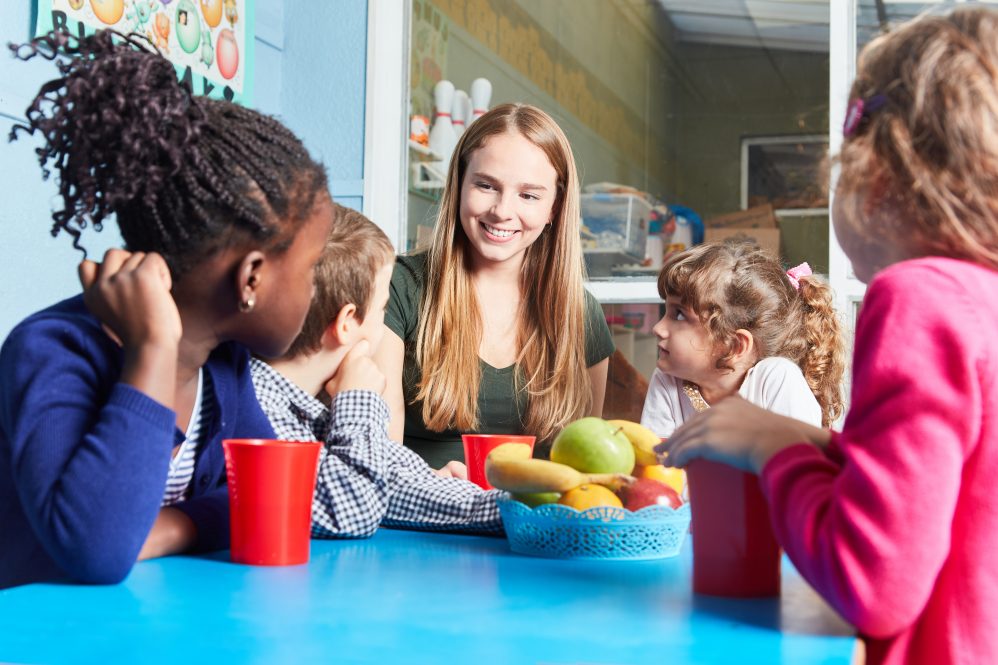 Children and carer together eat fruit as a snack in the kindergarten or daycare