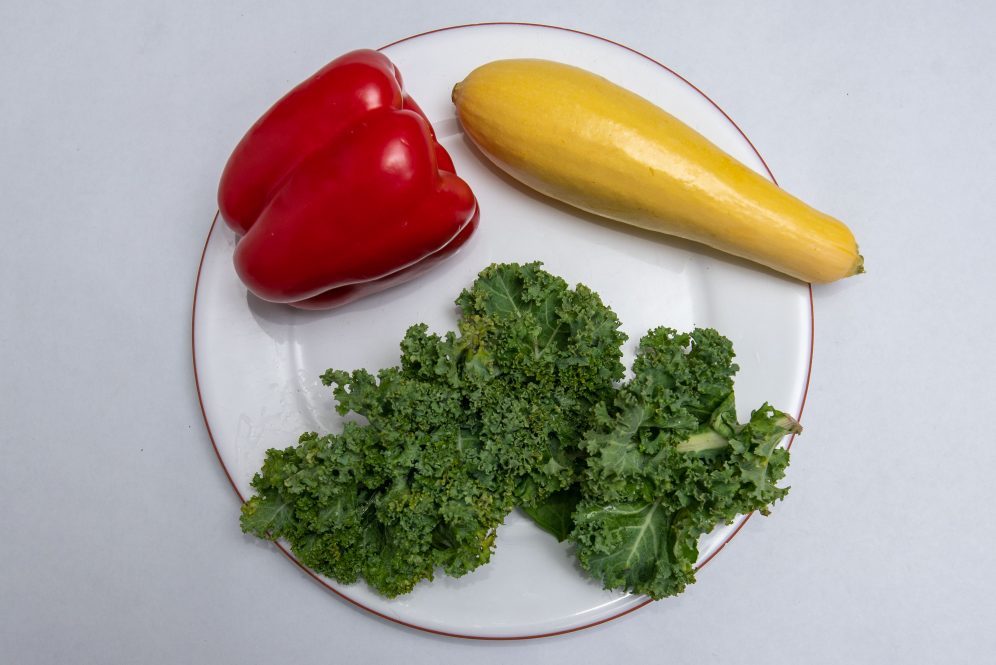 white plate with a red pepper, yellow squash and kale