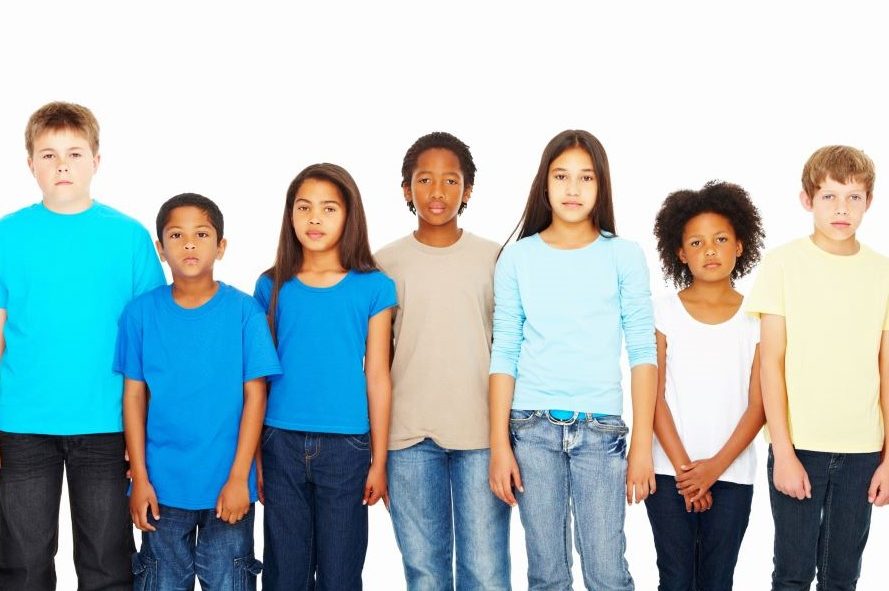 a group of diverse kids stand facing the camera with serious expressions. They are wearing blue jeans and shorts in varying shades of blue and neutral colors