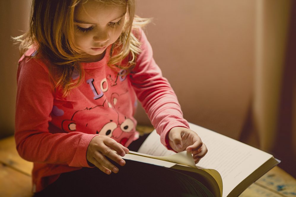 a toddler girl holds an open book on her lap and turns a page