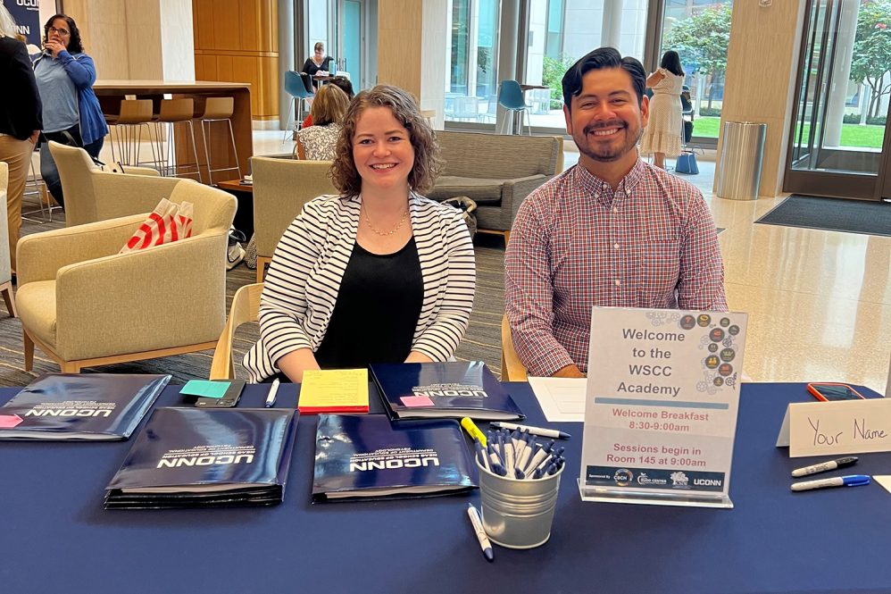 CSCH postdoc Kathleen Williamson and Rudd Center Research Assistant Joel Villalba sit at a table welcoming participants to the WSCC Academy. Photo credit: Carson Hardin, Rudd Center